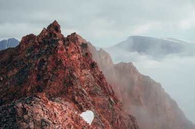 Bulutlu gökyüzünde sürreal uçlu kaya zirvesi. Canlı, sivri, kayalık bir tepe. Dev bir taş parçası. Atmosferik minimalist alp manzarası. Gökyüzünde keskin kayalık bir dağ tepesi. Muhteşem dağlık manzara.