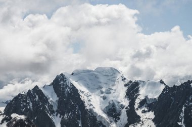 Atmosferik minimalist alp manzarası karlı dağ zirvesinde asılı devasa bir buzulla. Buzul sınırında büyük bir balkon. Karlı dağların üzerindeki bulutlu gökyüzü. Yüksek irtifada görkemli manzara.