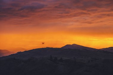 Atmosferik manzara. Dağların siluetleriyle. Arkasında ağaçlar olan. Günbatımının ya da aydınlatıcı rengin gün doğumunun olduğu renkli doğa manzarası. Günbatımı ödemesi