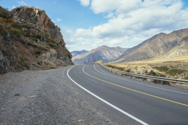Renkli sonbahar manzarası, gün ışığında kayalar boyunca uzanan dağ yolu. Sonbahar renklerinde dağ yolu olan parlak alp manzarası. Sonbahar zamanı dağlarda otoyol. Yol boyunca güzel kayalık duvar boyunca.