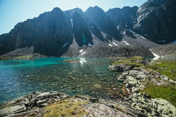 阳光普照的山水 绿油油的冰湖 阳光普照 绿松石清澈的高山湖水和大石头 美丽的风景 高山上的湖雪交融 石底在透明的水中 — 图库照片
