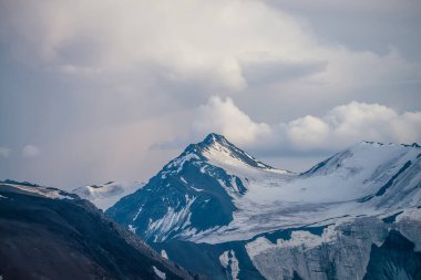 Bulutlu gökyüzünün altında, büyük, karlı dağ zirvesi mavi beyaz renklerle muhteşem dağlar. Atmosferik dağ manzarası, yüksek dağ duvarı, beyaz bulutların altında kar var..