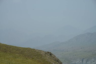 Asgari sisli ve beyaz sisli yeşil dağları olan bir yer. Dağ geçidinden yeşil vadiye ve beyaz sisli büyük dağlara minimalist bir manzara. Atmosferik sisli minimalizm. Dağlar ve kayalar sisli