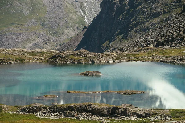 Turkuazda yosunlu taş güneş ışığında dağ gölünün berrak suyu. Güneşli doğa manzarası. Büyük kayanın arka planında gök mavisi bir buzul gölü var. Atmosferik dağ manzarası.