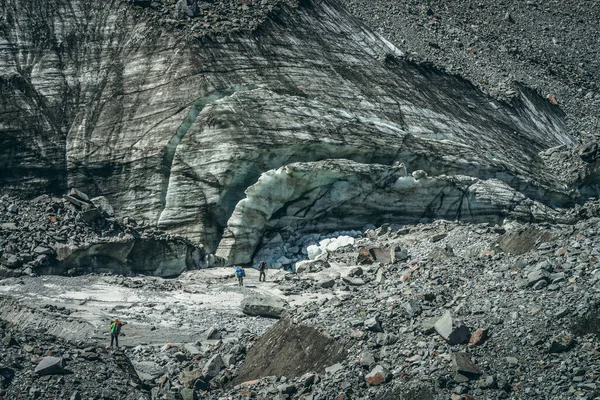 砕けた氷河の氷のブロックの間でハイカーと風景の山の風景 大規模なモレーンの間でバックパックを持つ観光客や山の傷を持つ大きな氷河の氷塊と美しい風景 — ストック写真