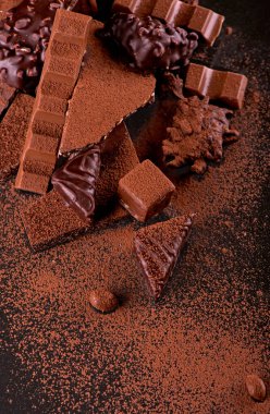 Kırık çikolata parçaları ve tahta arka planda kakao tozu.