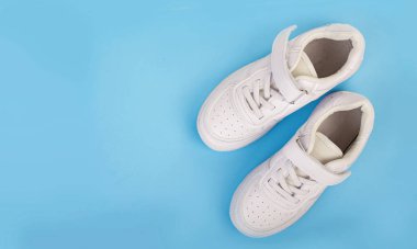 Mavi arka planda izole edilmiş bir çift beyaz deri spor ayakkabı..