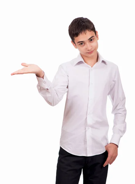 El chico sonriente con ropa blanca sobre un fondo blanco mira a la cámara y muestra una palma vacía. Joven alegre en camisa blanca se muestra en el espacio en blanco — Foto de Stock