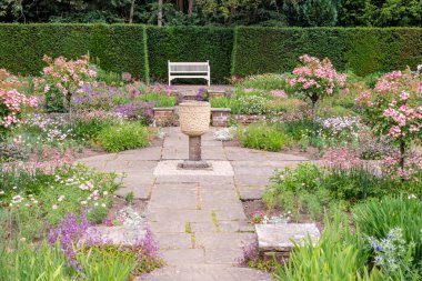 Bayraklı İngiliz resmi bahçesinin huzurlu köşesinde çiçek yatakları ve taş bir vazo. 