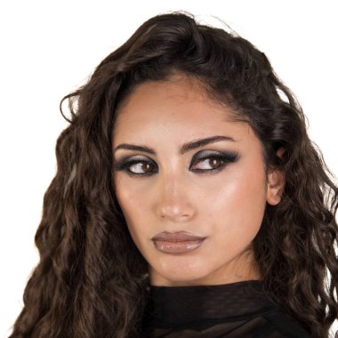 Genç esmer, kıvırcık saçlı, modern dumanlı göz makyajı yapan, şık bir stüdyo fotoğrafında parlak dudaklı, kendinden emin bir şekilde başka tarafa bakan.