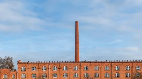 Old factory in orange brick with giant chimney.