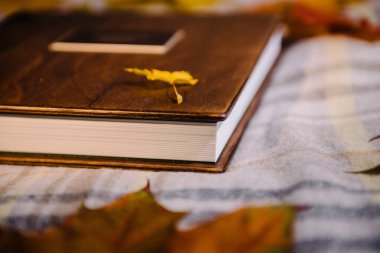 Kalın bir kitabın köşesinde beyaz deri kaplı sayfalar ve sarı akçaağaç yapraklarının arasında masa örtüsünün üzerinde doğal bir ahşap kapak. Kitabı kapat.