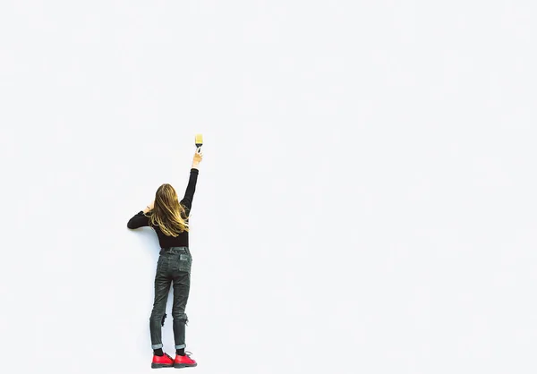 Genç bir kız ışık duvarında bir fırçayla resim çizer.