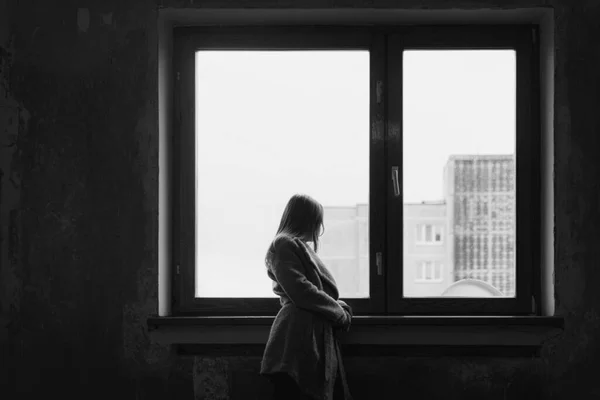 Eski bir pencerenin yanında duran ve kalın kıyafetler giymiş genç bir kızın renkli görüntüsü.