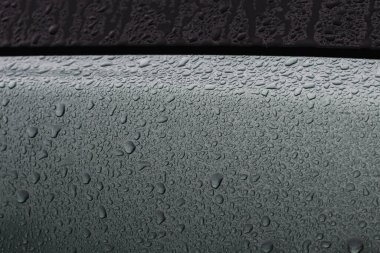 Koyu renkli bir arabanın yağmur damlalarıyla kaplı bir parçası.