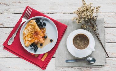 Dekoratif beyaz bir masada bir fincan kahve ve bir tabak krep.