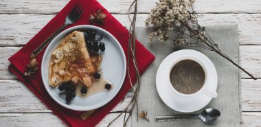 Dekoratif beyaz bir masada bir fincan kahve ve bir tabak krep.