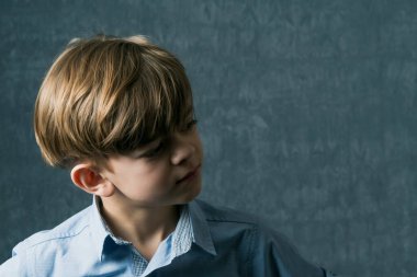 Gömlekli kahverengi gözlü küçük bir çocuk kameraya poz veriyor. Karanlık bir arka planda