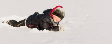 Sıcak giysili küçük bir çocuk güneşli bir günde karda oynar.