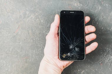 Yetişkin biri akıllı telefonu kırık bir ekranla tutar.