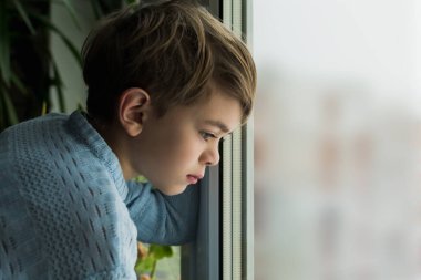 Küçük bir çocuk üzüntülü bir şekilde pencereden dışarı bakıyor.