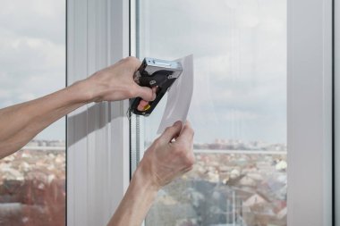 Adamın biri bir kağıt parçasını zımbayla pencereye tutturmaya çalışıyor.