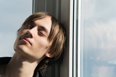 Güneşli bir günde pencerenin yanında genç bir adamın portresi.