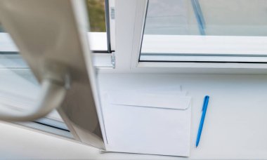 Açık bir pencerenin pervazında bir mektup ve bir kalem.