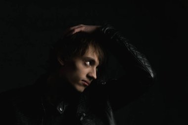 Çok koyu bir arka planda uzun saçlı bir gencin portresi.