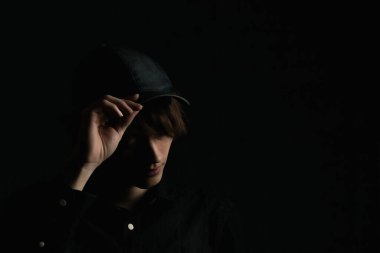 Çok koyu bir arka planda uzun saçlı bir gencin portresi.