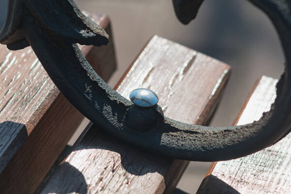 Фрагмент черной металлической части деревянной скамейки в парке.