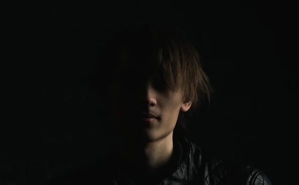 Portrait image of a young guy with long hair on a very dark background