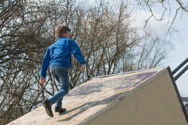 Küçük bir çocuk, metal halatlarla asma köprünün yanında parkta yürüyor.