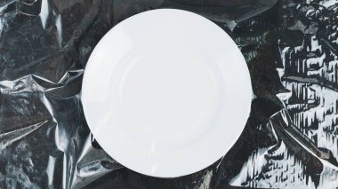 Dekoratif bir arka planda plastik ambalajla kaplı beyaz tabak