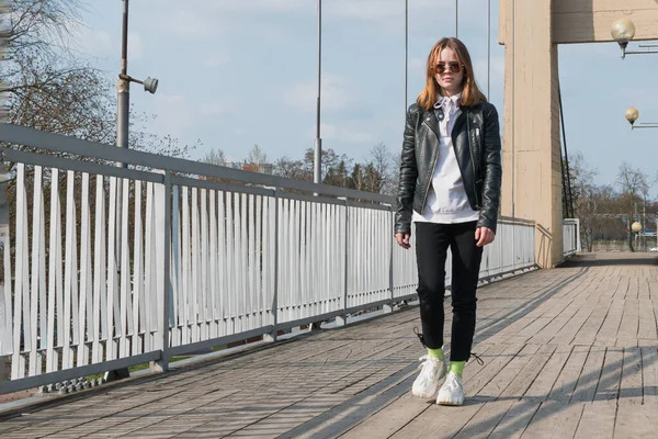 一个戴着时髦眼镜 穿着皮夹克的小女孩在一座悬吊的人行天桥上 — 图库照片