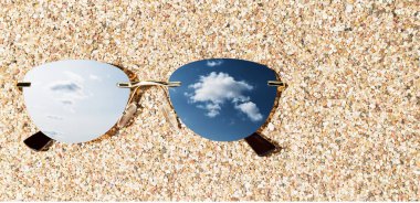 Güneş gözlükleri kumsalda güneşli gökyüzünün yansımasıyla uzanıyor.