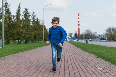 Küçük bir çocuk parkın yakınındaki bir pistte koşuyor.