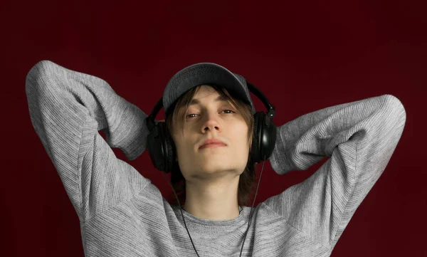 髪の長い若い男は 赤い背景にヘッドフォンで音楽を聴く — ストック写真