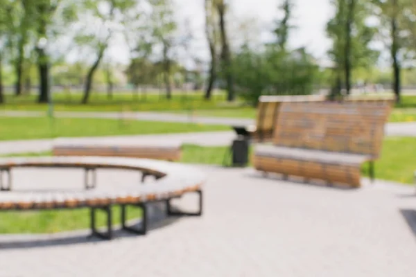 A blurry image of a city park in summer with wooden decorative benches