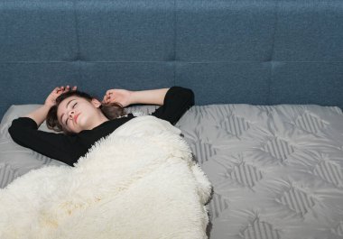 Genç bir kız yeni beyaz bir battaniyeyle kaplı yeni bir yatakta yatıyor.