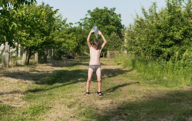 Küçük bir çocuk sıcak havada plastik bir şişeden suyla kendini ıslatıyor.