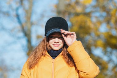 Güneşli bir sonbahar parkında şapkalı ve sarı ceketli genç bir kız.