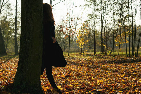 A young girl in a yellow jacket walks in an autumn park with fallen leaves
