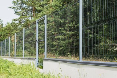 Ormanın yakınında kapısı ve kilidi olan metal bir çit.