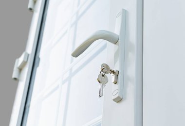 Beyaz bölümleri olan yeni plastik bir pencere ve bir kır evinde kilitli bir kapı kolu.