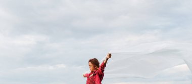 Kırsal bir akşam manzarasının arka planında büyük bir beyaz materyal parçasıyla genç bir kızın görüntüsü.