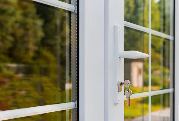 Beyaz bölümleri olan yeni plastik bir pencere ve bir kır evinde kilitli bir kapı kolu.