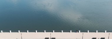 Parktaki setin yanındaki geniş bir nehrin üst manzarasında bir adam ve bir kadın suya bakıyorlar.