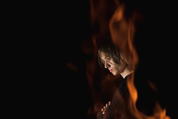 The view of an adult guy with long hair through the fire in complete darkness