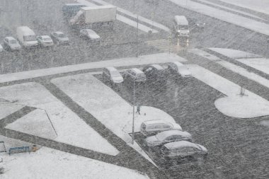 Kışın kar fırtınası sırasında arabalarla dolu bir otoparkın bulanık görüntüsü.